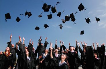 newly graduated people wearing black academy gowns throwing hats up in the air